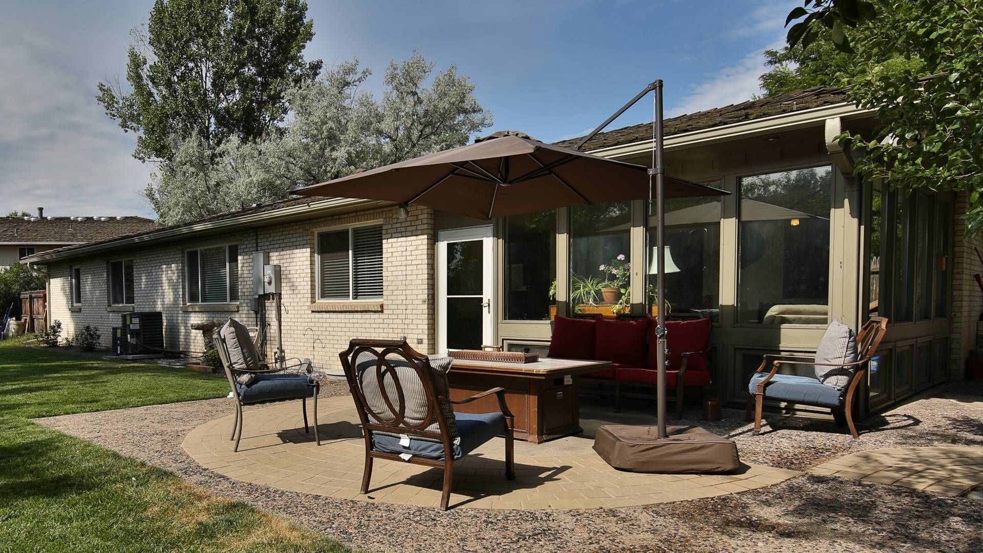 Patio with umbrella, table, chairs, and a bench outside a house.