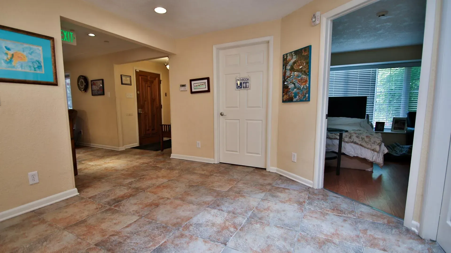 Hallway with tile floor, white door, and doorway to bedroom. Paintings hang on the walls.