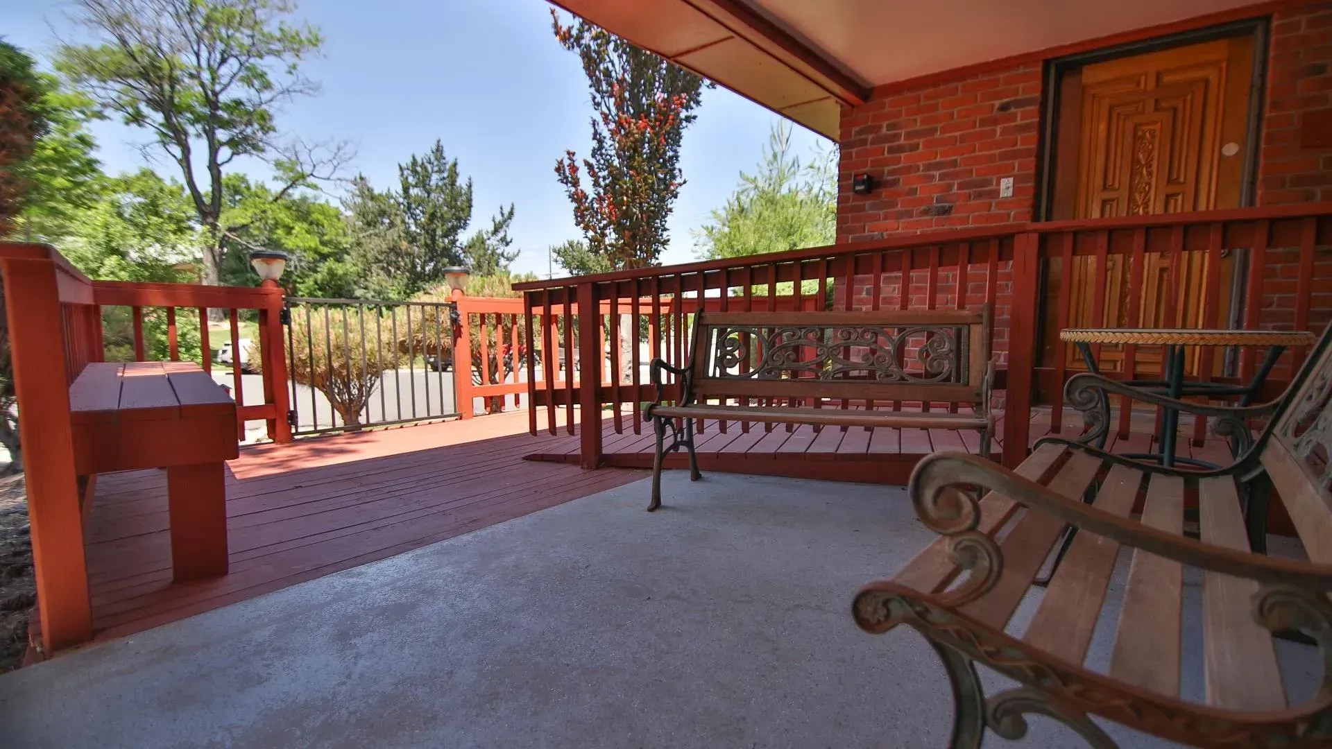 Red brick porch with a bench, small table, and railing.