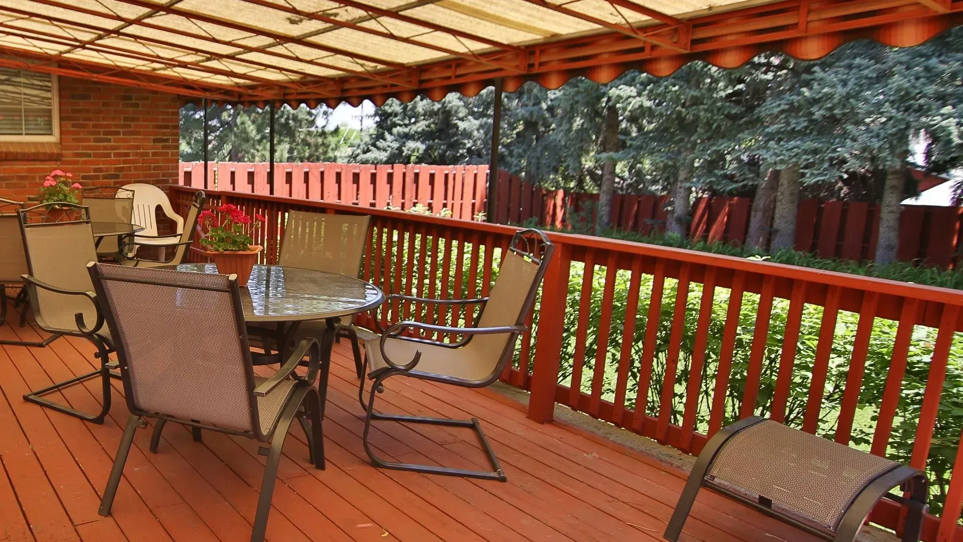Deck with patio furniture, red railing, brick house, and trees.
