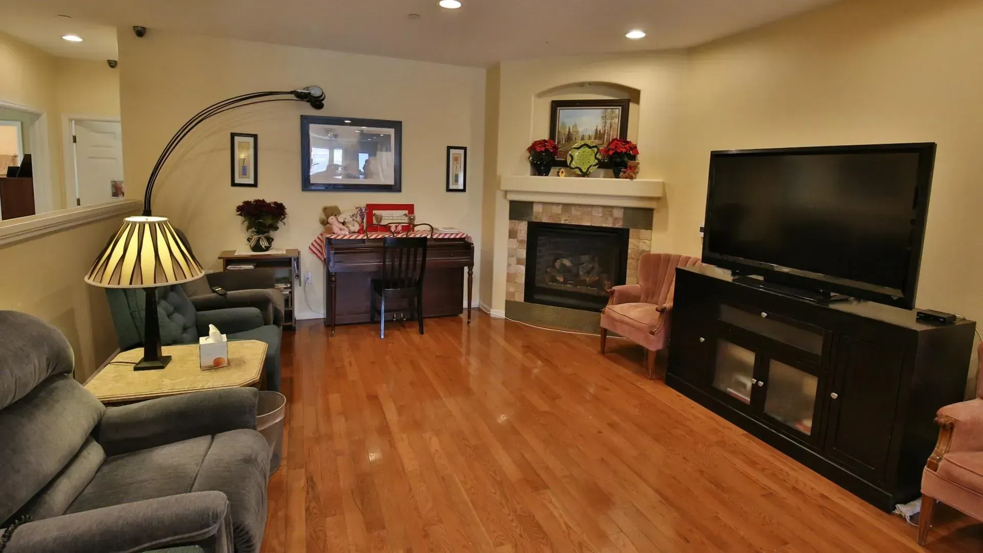 A cozy living room with fireplace, TV, chairs, and hardwood floors; warm tones and soft lighting.