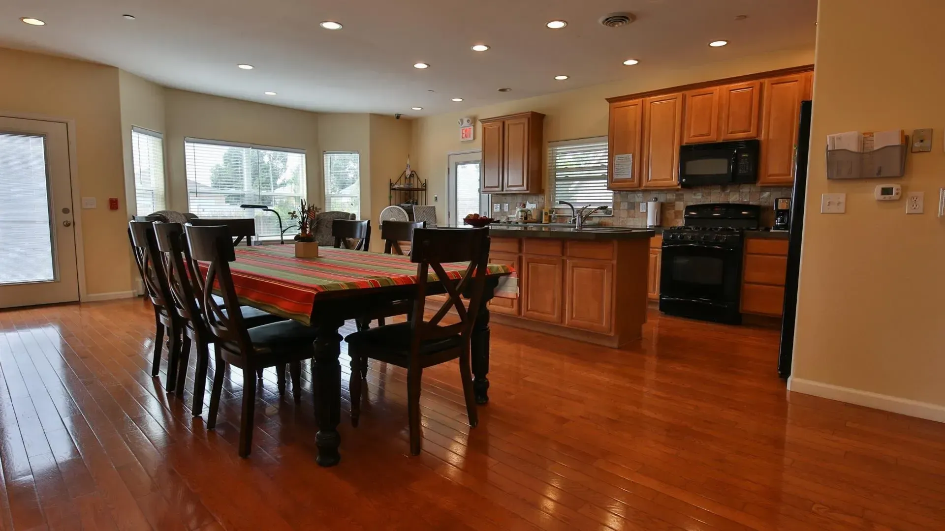 Spacious dining room with a table, chairs, and kitchen with wood cabinets and floors.