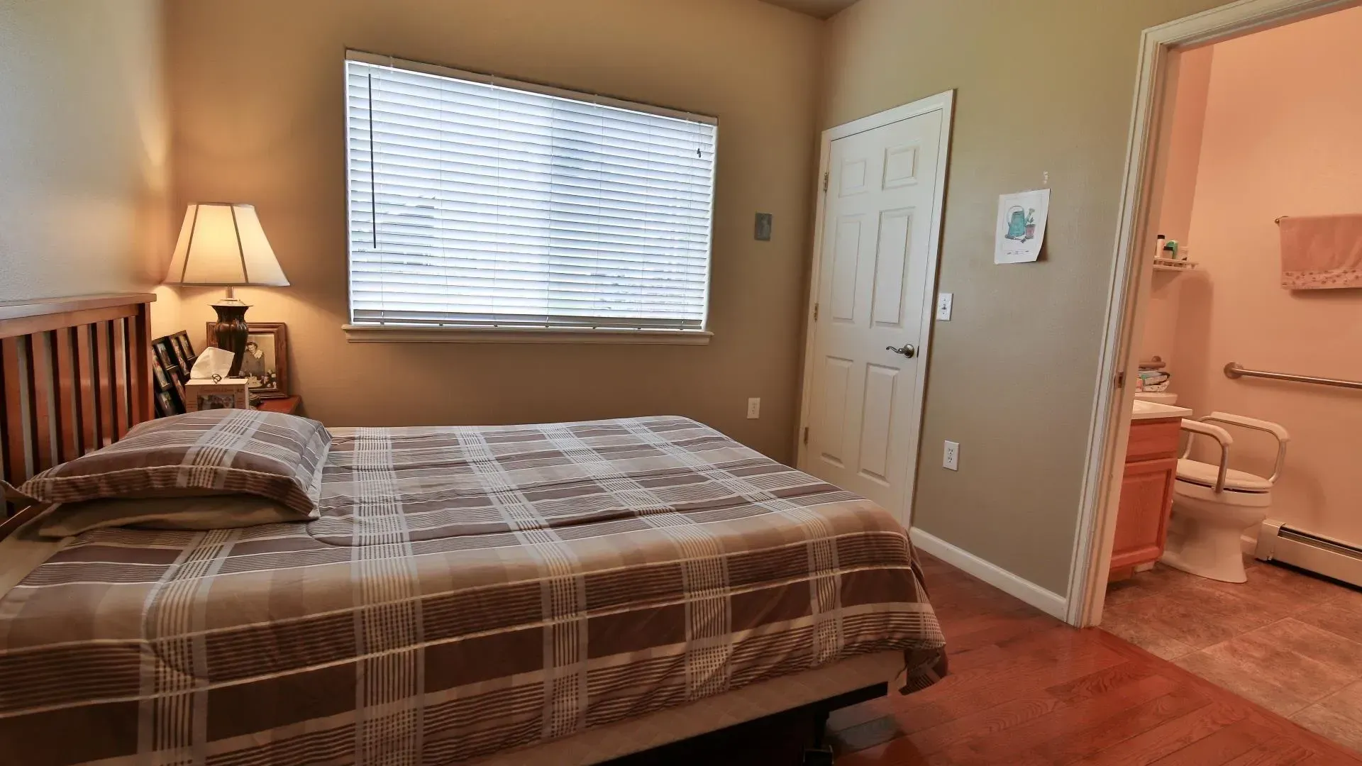 Bedroom with bed, window, lamp, and doorway to bathroom with grab bars.