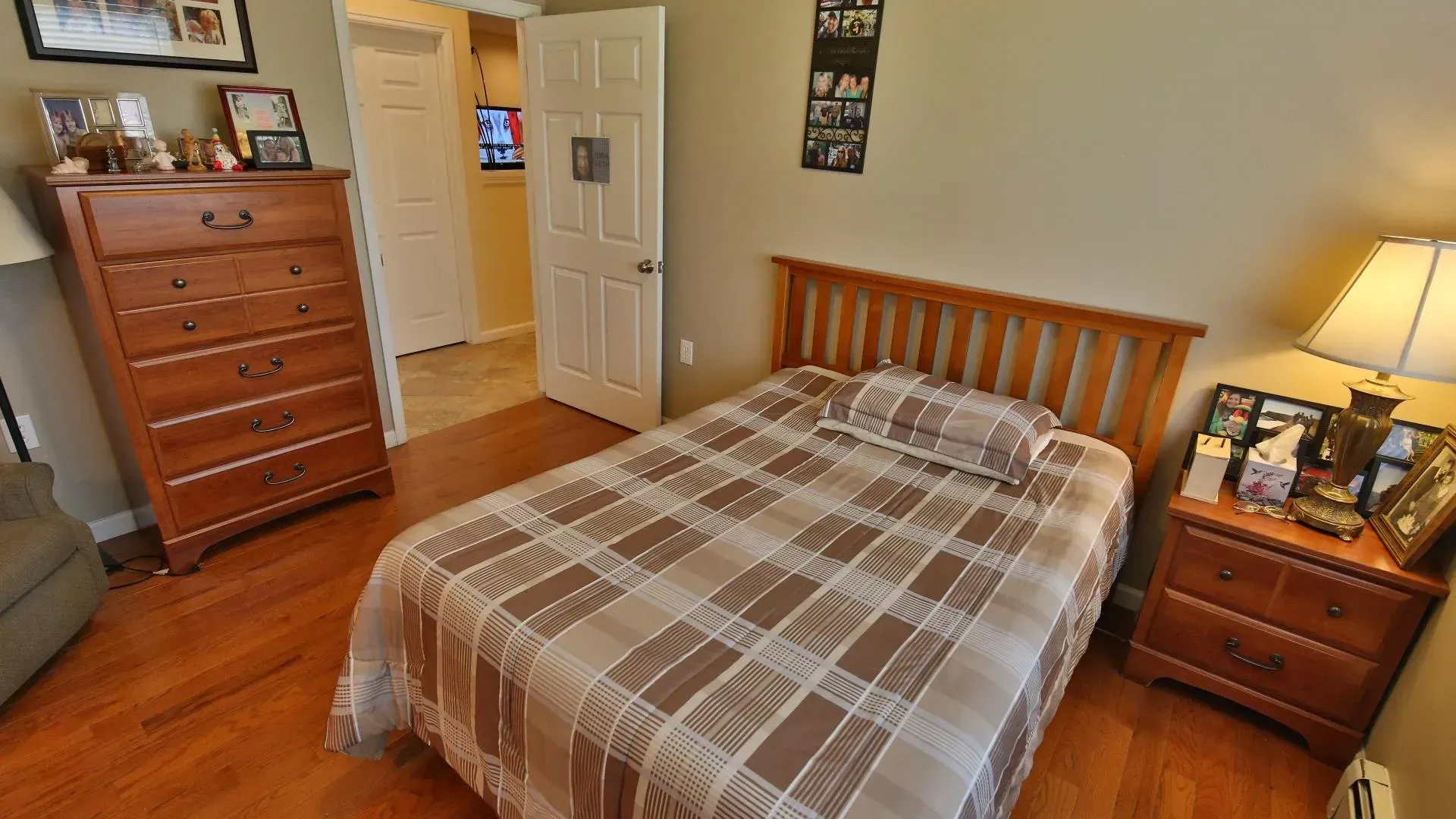 Bedroom with bed, dresser, and nightstand on hardwood floor. Doorway to another room.