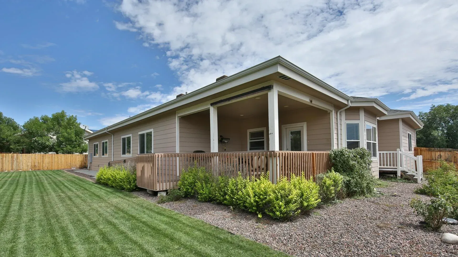 Backyard with a house, green grass, wooden fence, and blue sky with clouds.