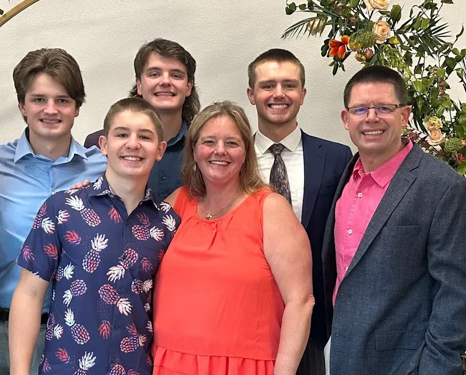 Family of six smiling for a photo. A woman and man stand with their four sons.