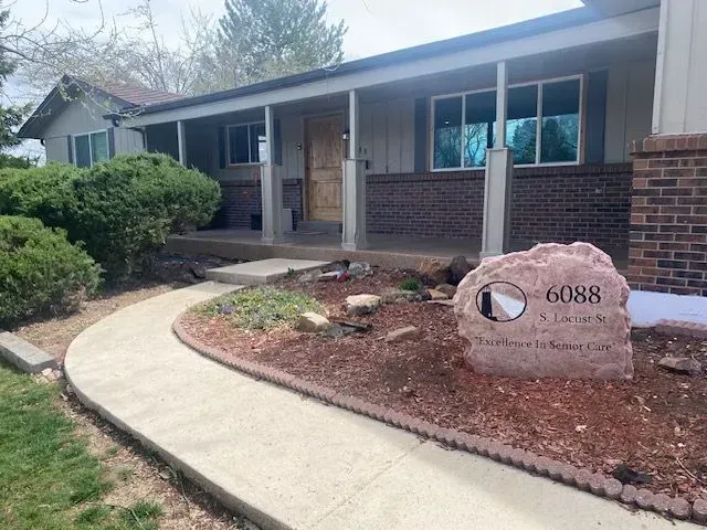 A single-story house with a covered porch, a stone address marker, and a winding sidewalk.