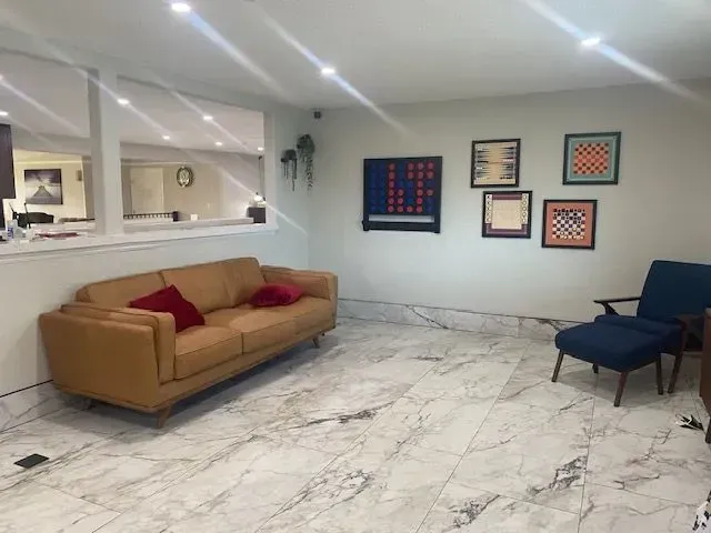 Living room with tan sofa, blue chair, decorative game boards on the wall, and marble flooring.