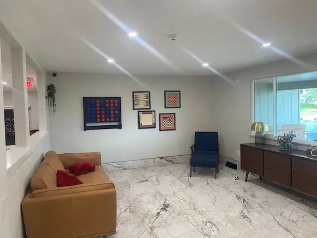 Modern living room with tan couch, blue chair, art, marble floor, and a window.