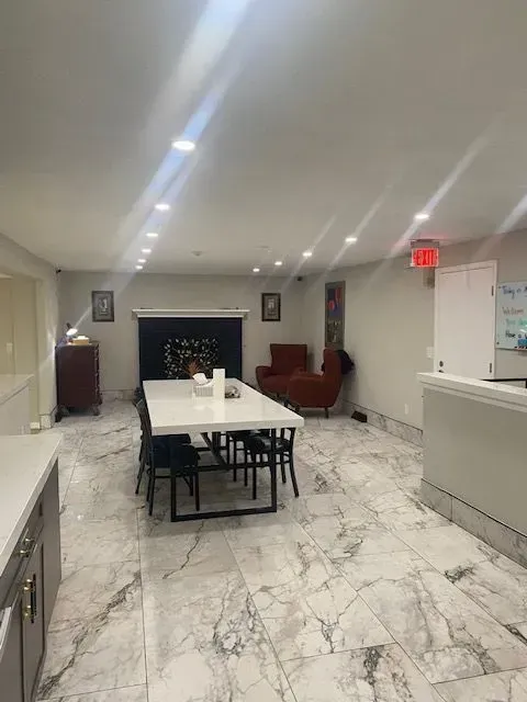 Spacious room with white marble tile floors, long table, fireplace, red sofa, and white walls.