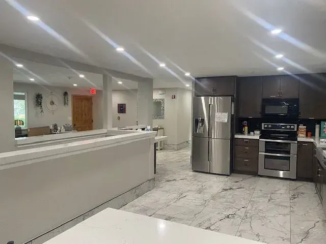 Kitchen with stainless steel appliances, dark cabinets, marble floors, and a white countertop.