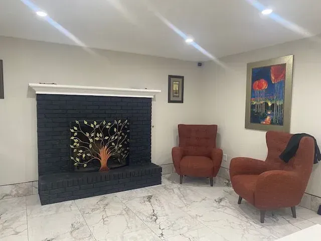Living room with black brick fireplace, orange armchairs, art, and white marble floor.