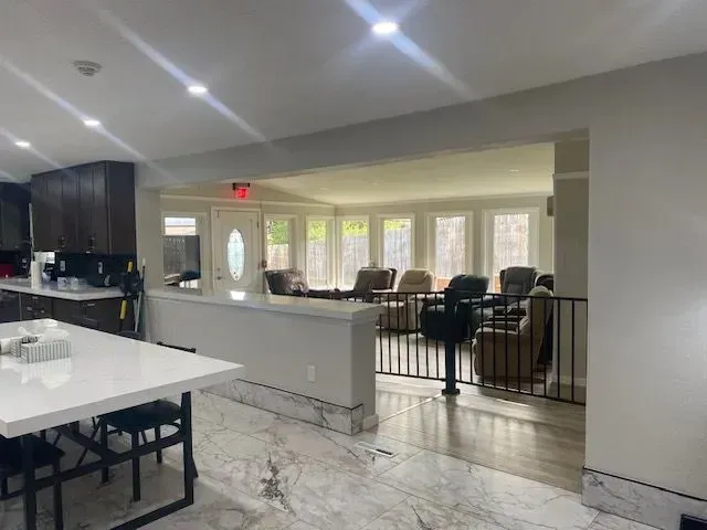 Open-concept room with kitchen, dining, and living areas. White and gray tones dominate the space.