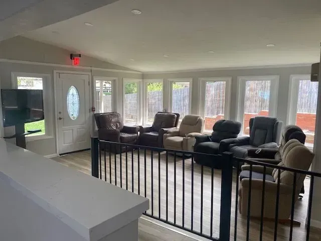 An open room with several recliners, a door, windows, and a TV.