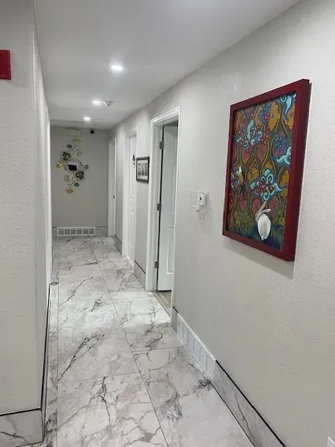 Hallway with marble flooring, artwork, and white walls.