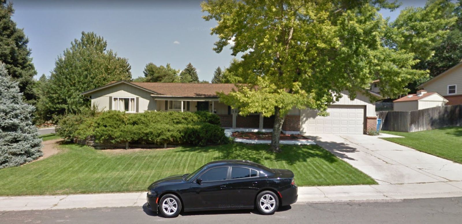 Black car parked in front of a house with a lawn and trees on a sunny day.