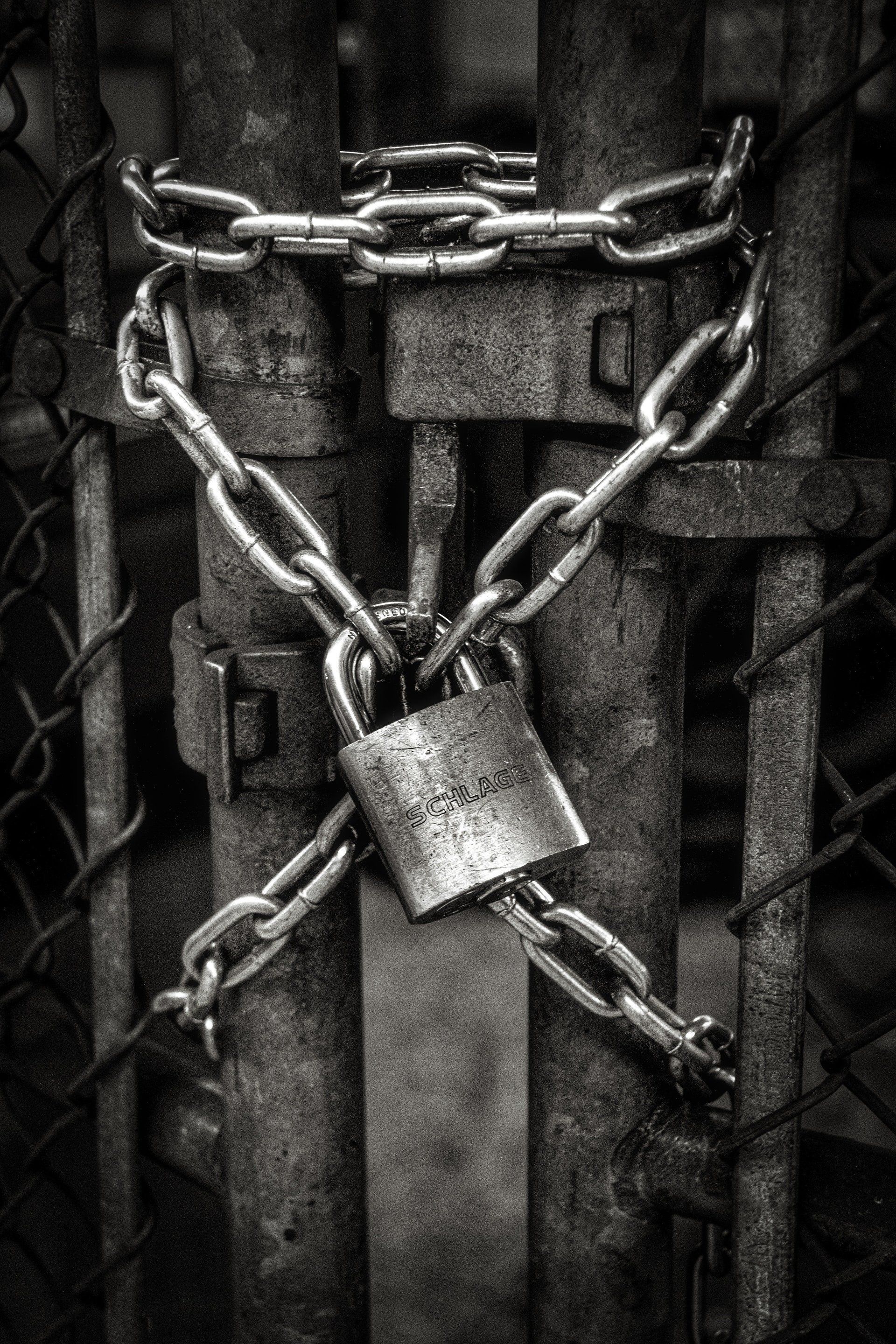 Grayscale shot of a weathered metal gate secured with chain and padlock.