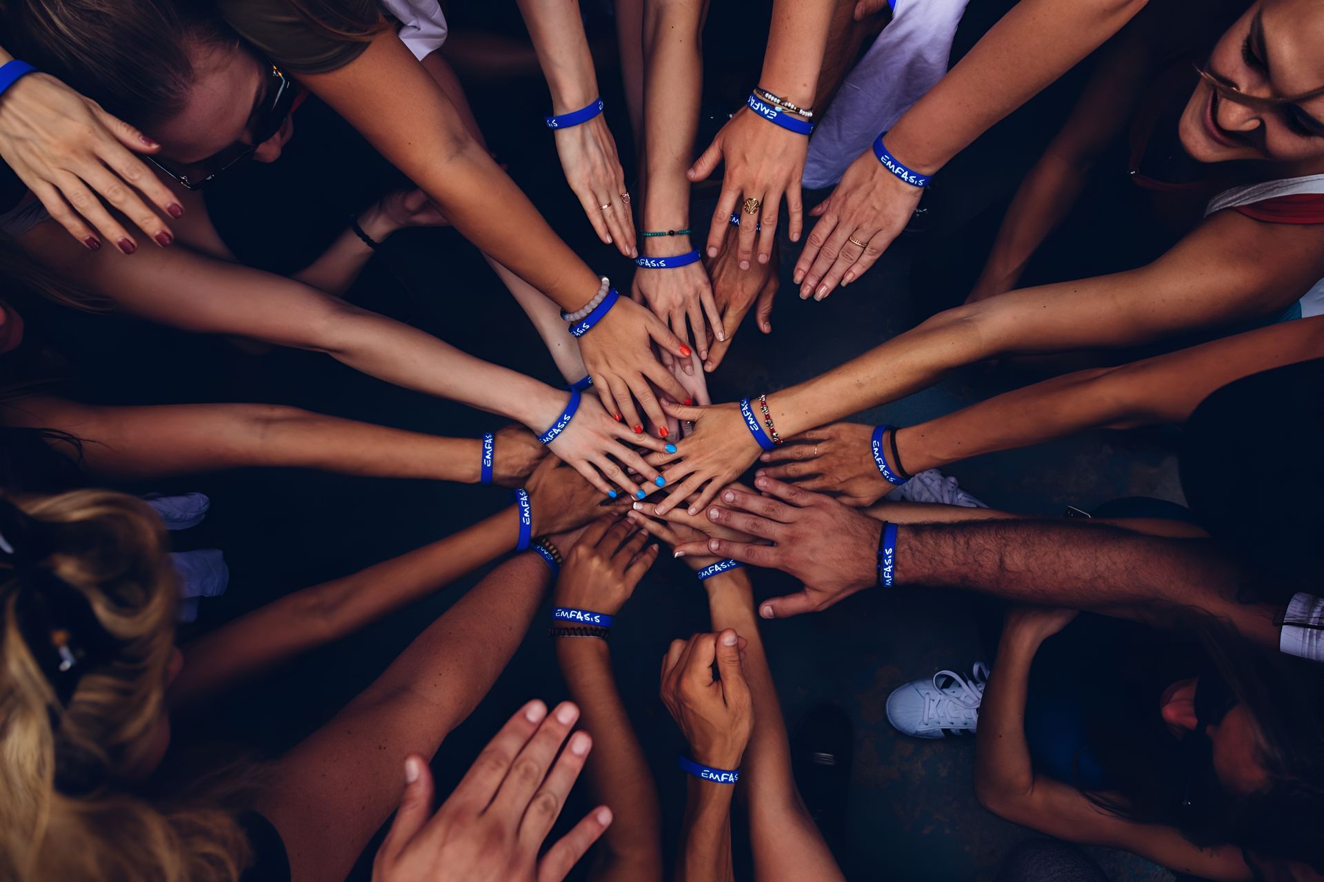Hands of diverse people in a circle, stacked together, wearing blue bracelets.