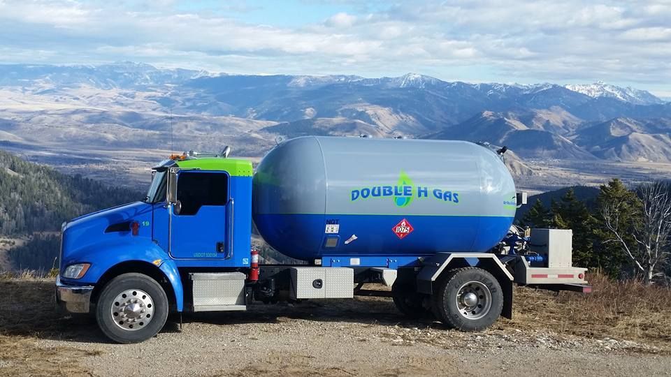 A blue and gray tanker truck is parked on top of a dirt hill.