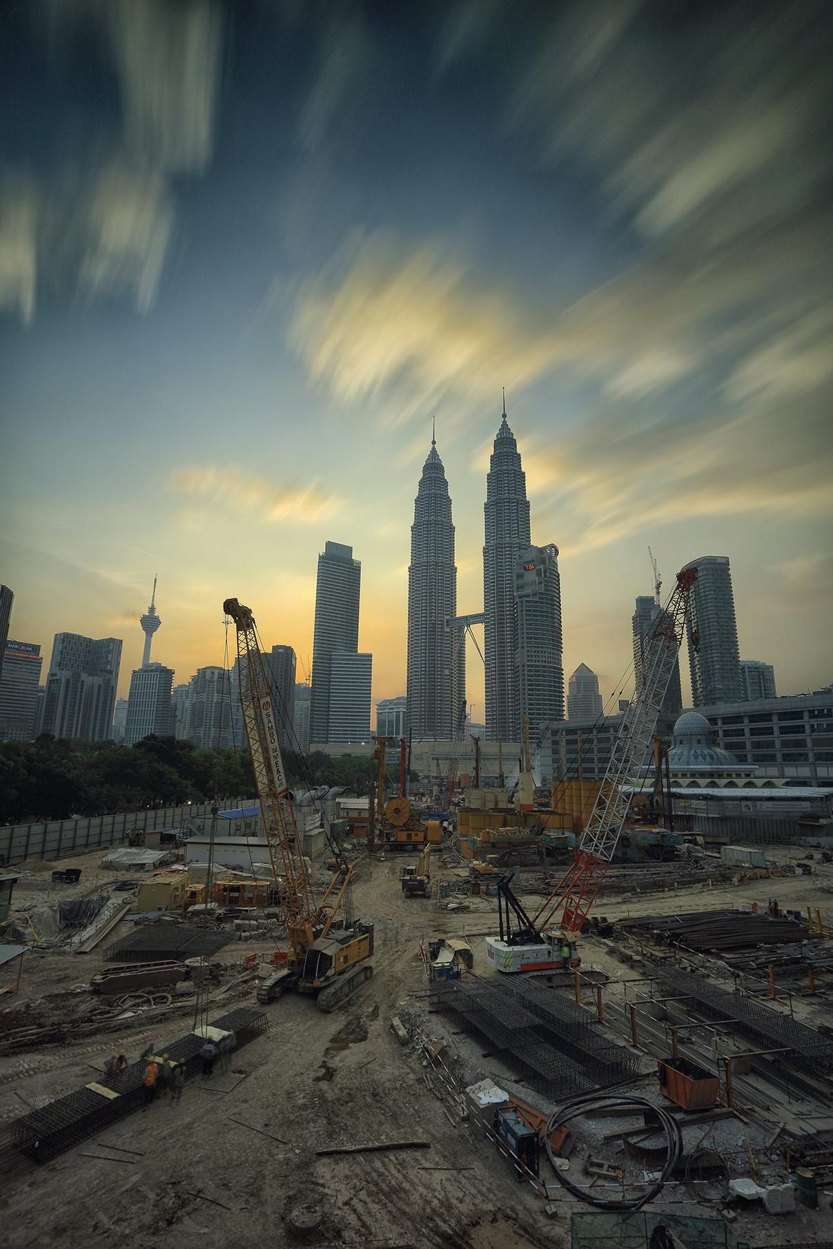 Kuala Lumpur skyline at sunset, including Petronas Towers and construction site in foreground.