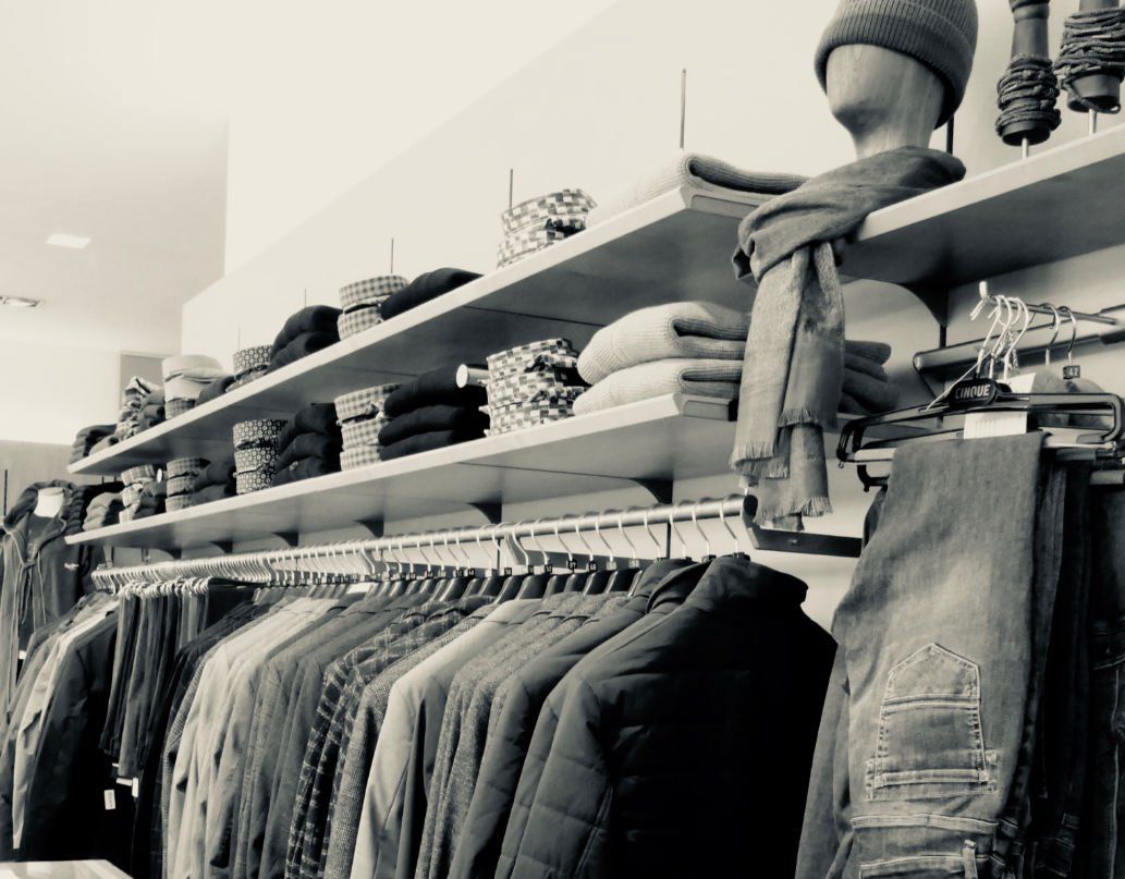 Ein Schwarzweißfoto von Kleidung, die in einem Geschäft an Kleiderständern hängt