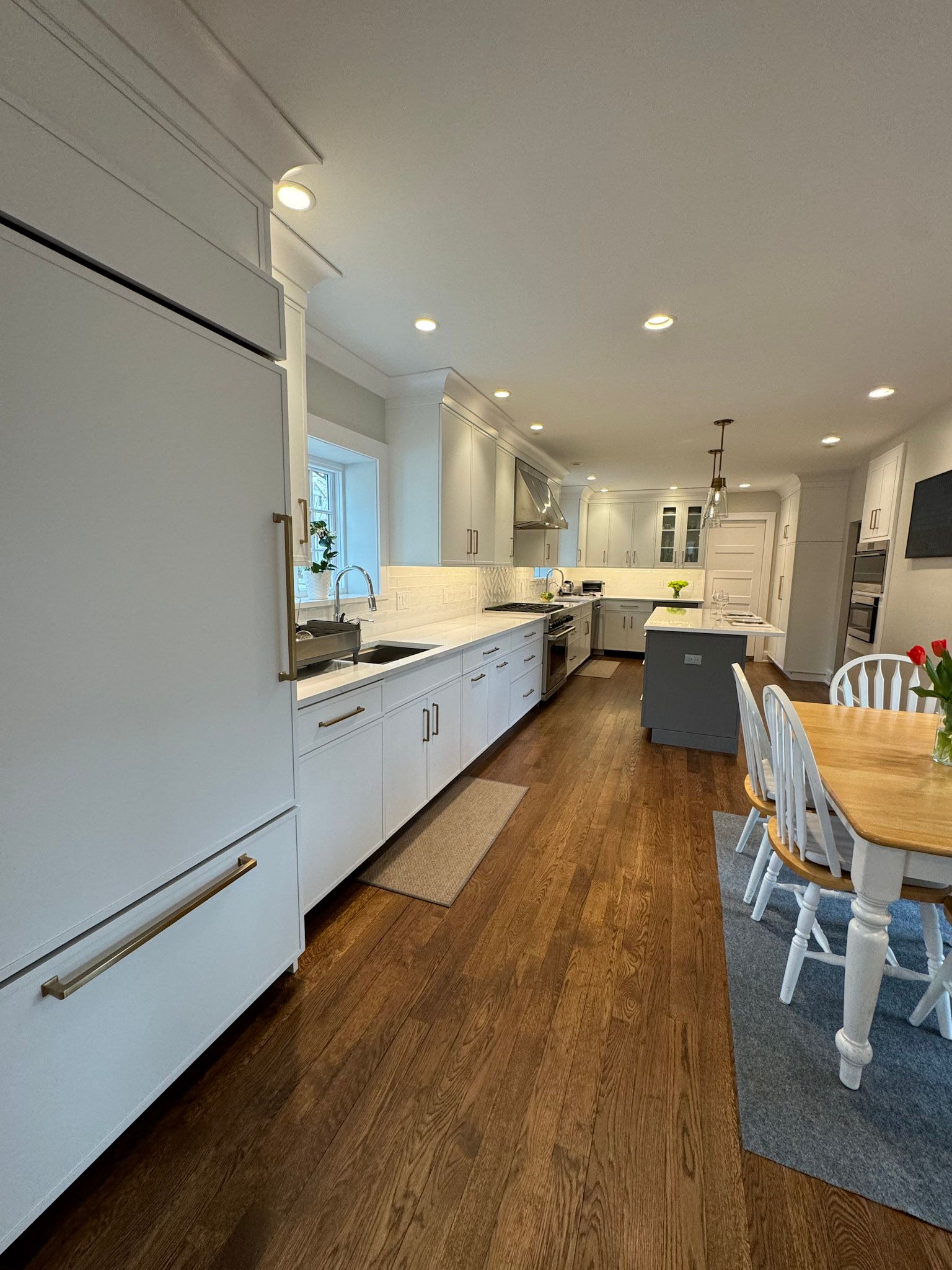 a kitchen with white cabinets , hardwood floors , a table and chairs .