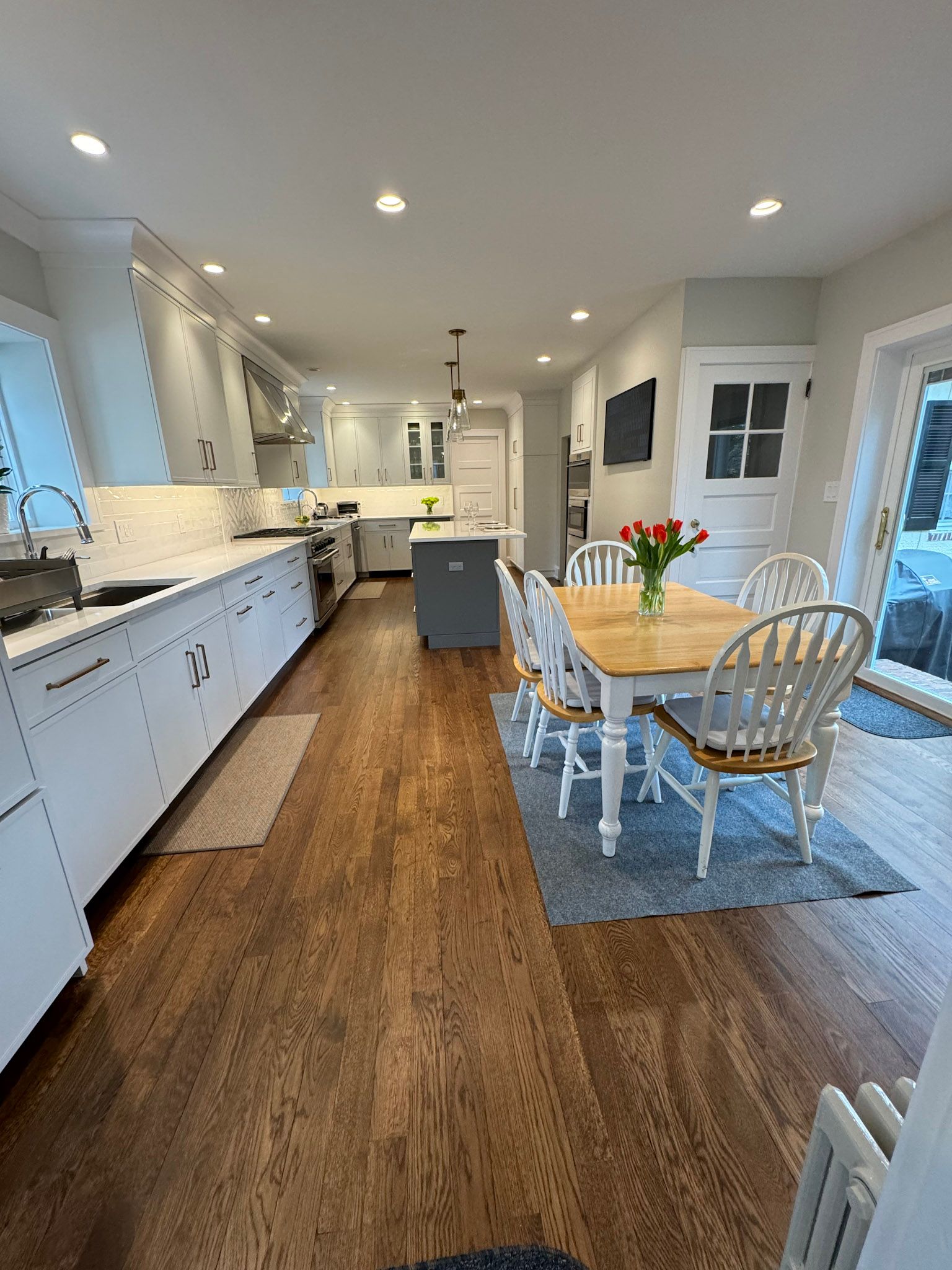 a kitchen with white cabinets , wooden floors , a table and chairs .