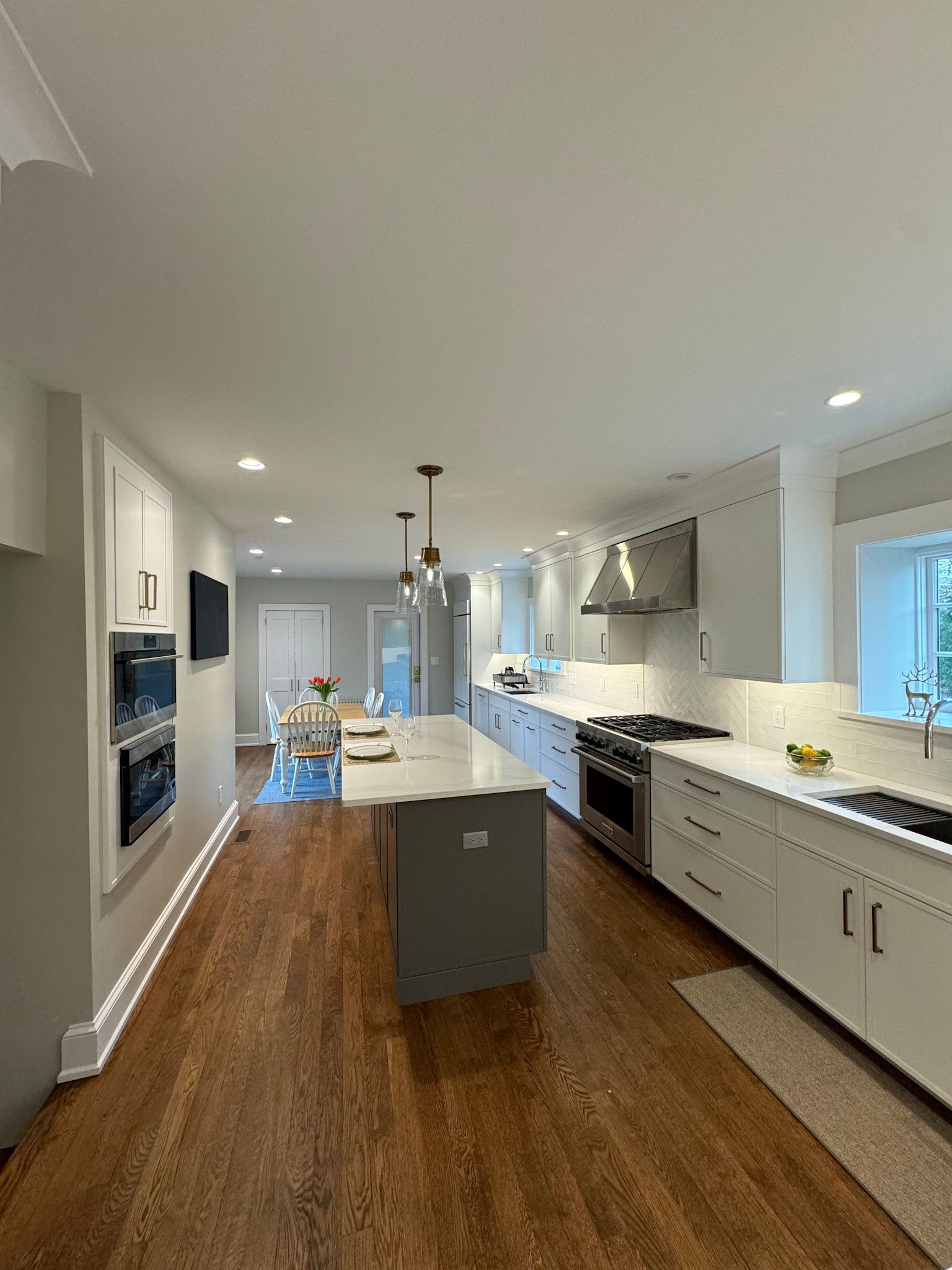 a kitchen with white cabinets , stainless steel appliances , hardwood floors and a large island .