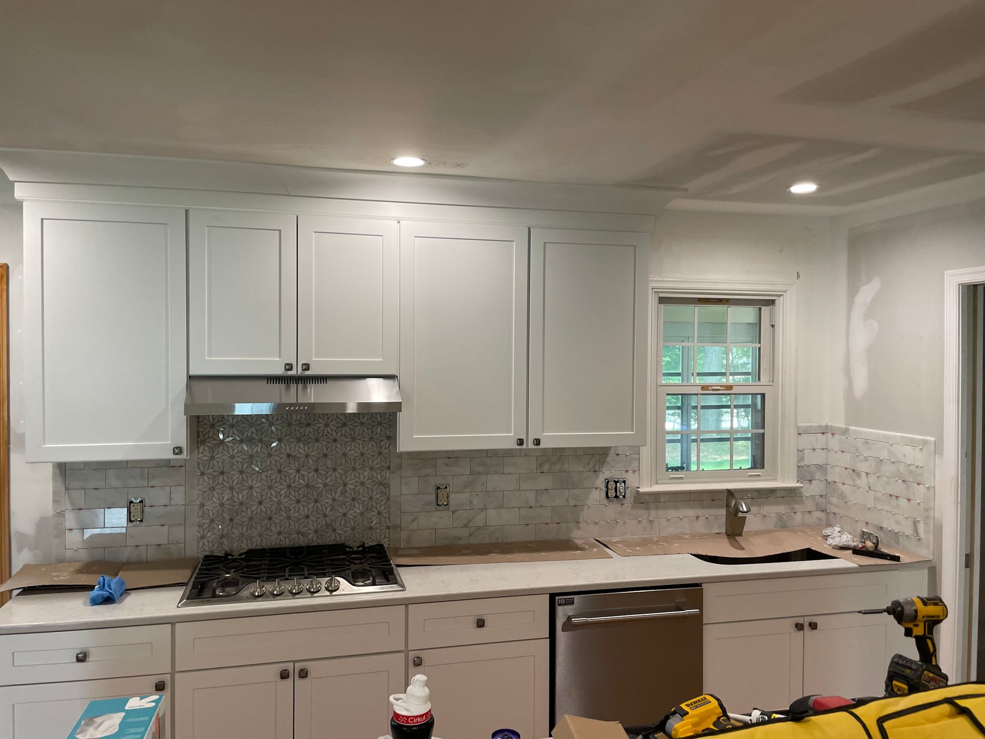 a kitchen with white cabinets , a stove , a dishwasher and a window .