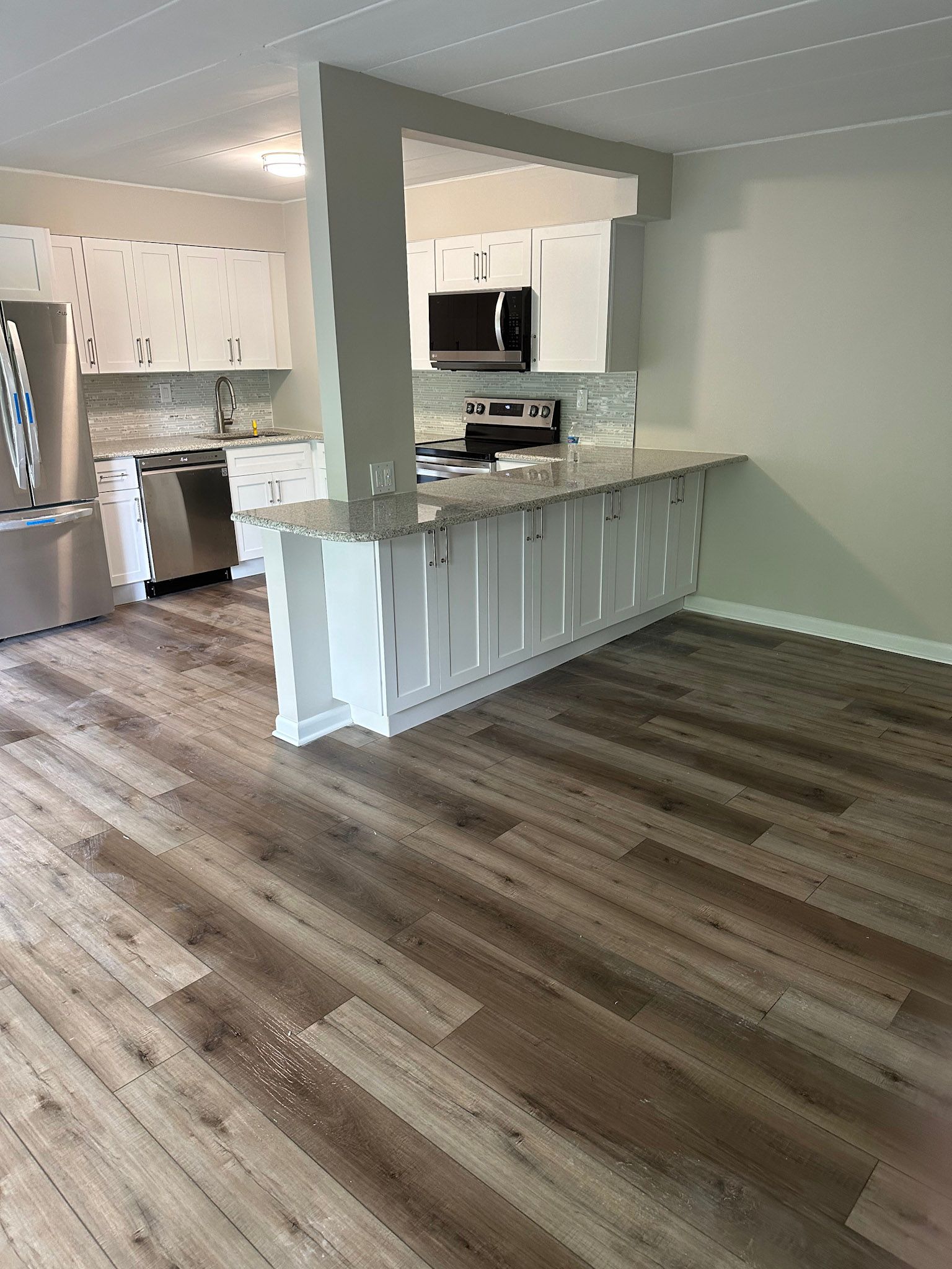 a kitchen with hardwood floors , white cabinets and stainless steel appliances .
