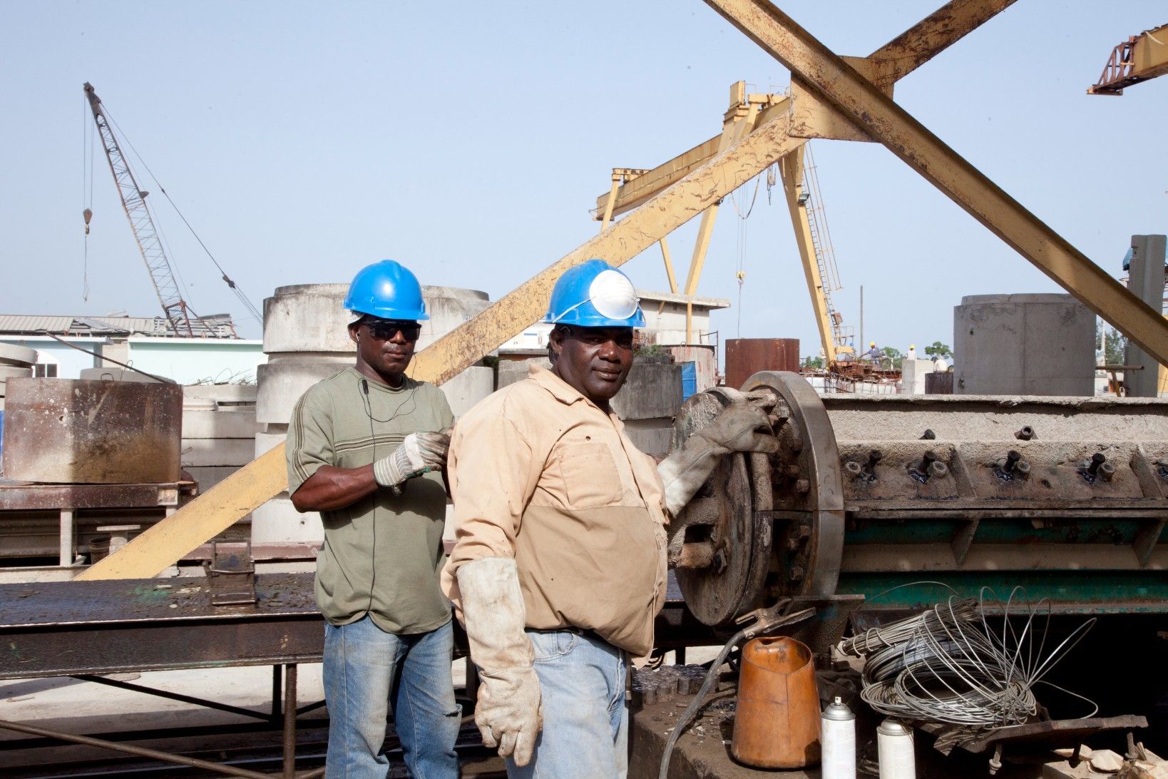 Two workers in blue hard hats stand beside industrial machinery at a construction site.