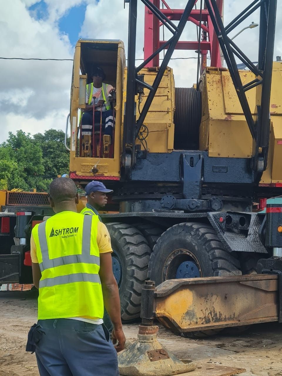 Worker in yellow safety vest stands beside a large drilling machine at a construction site.