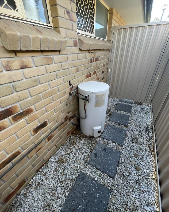 White Water Heater is Sitting Next to a Brick Wall — Luke Barry Plumbing in Southport, QLD