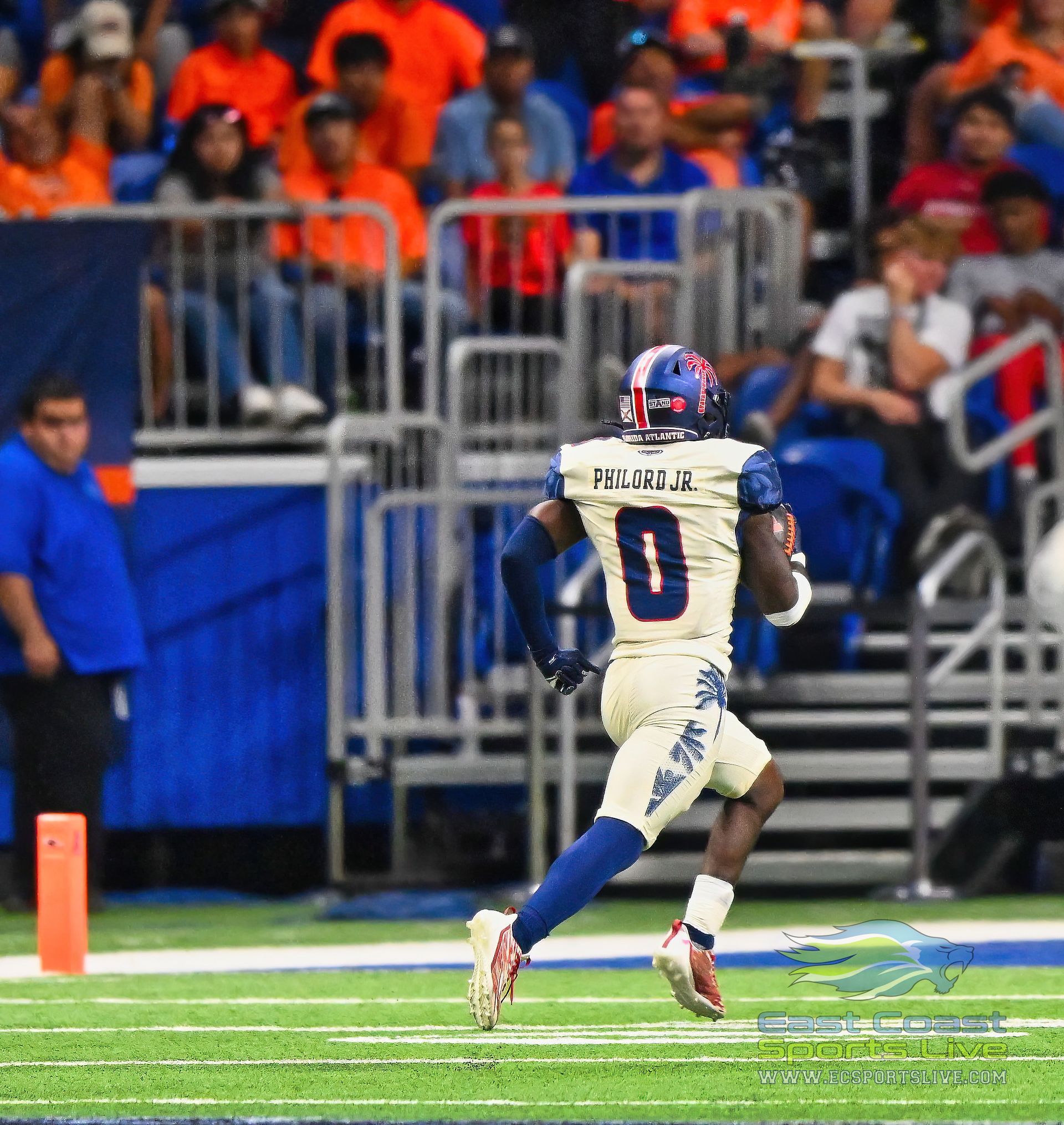 Football player in gold and blue uniform running on field, spectators in background.