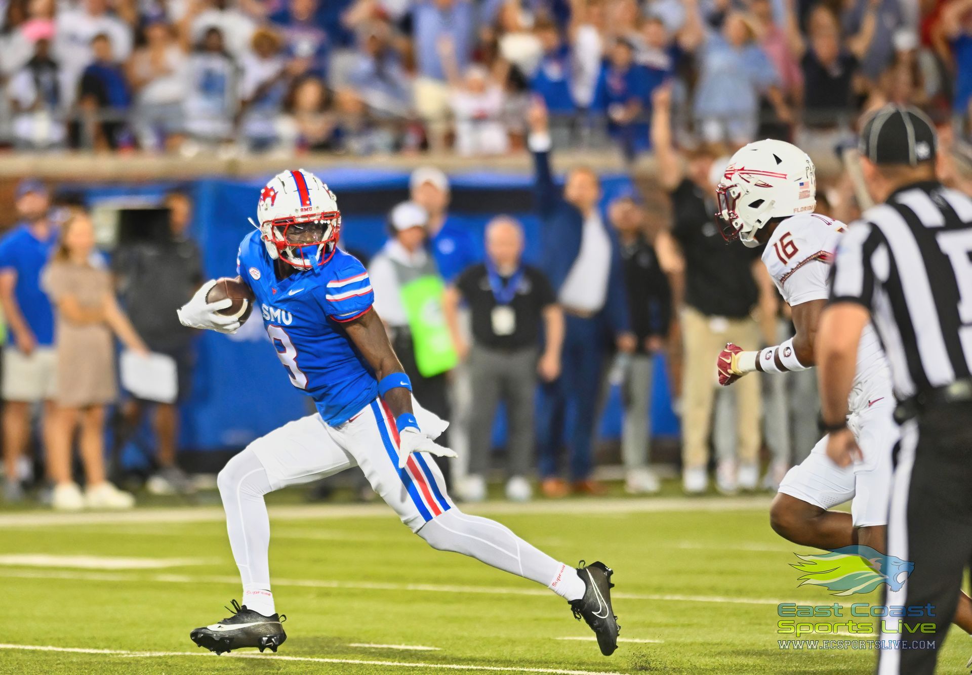 A football player is running with the ball while a referee watches.