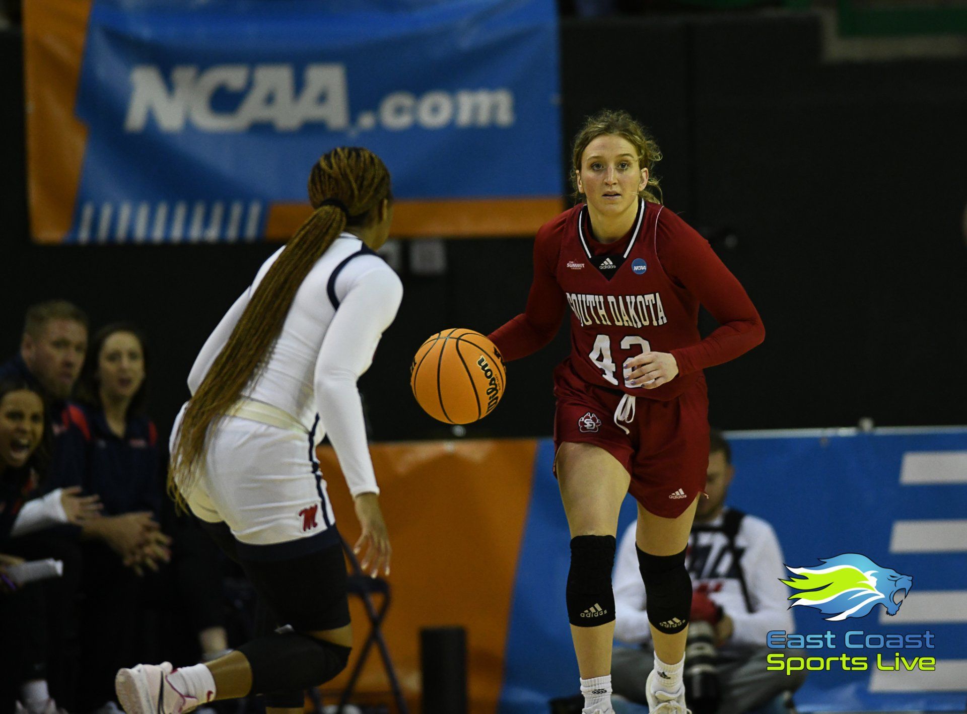 Two women playing basketball in front of a banner that says ncaa.com