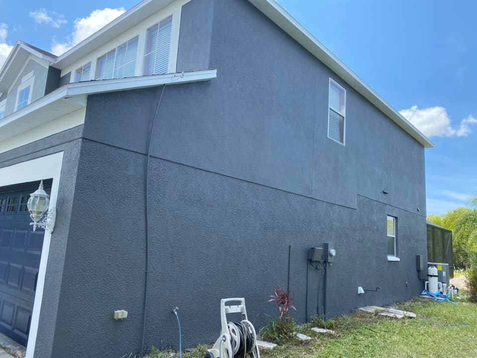 Gray house exterior with a garage, windows, and a pressure washer on the ground.