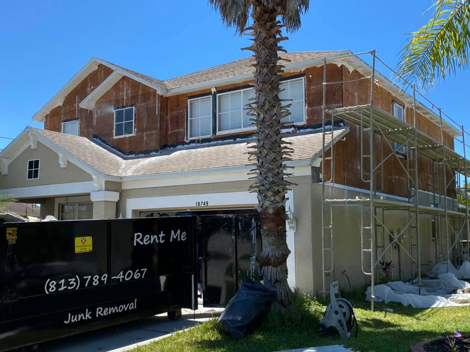 Two-story house under renovation with scaffolding, a dumpster, and a palm tree.