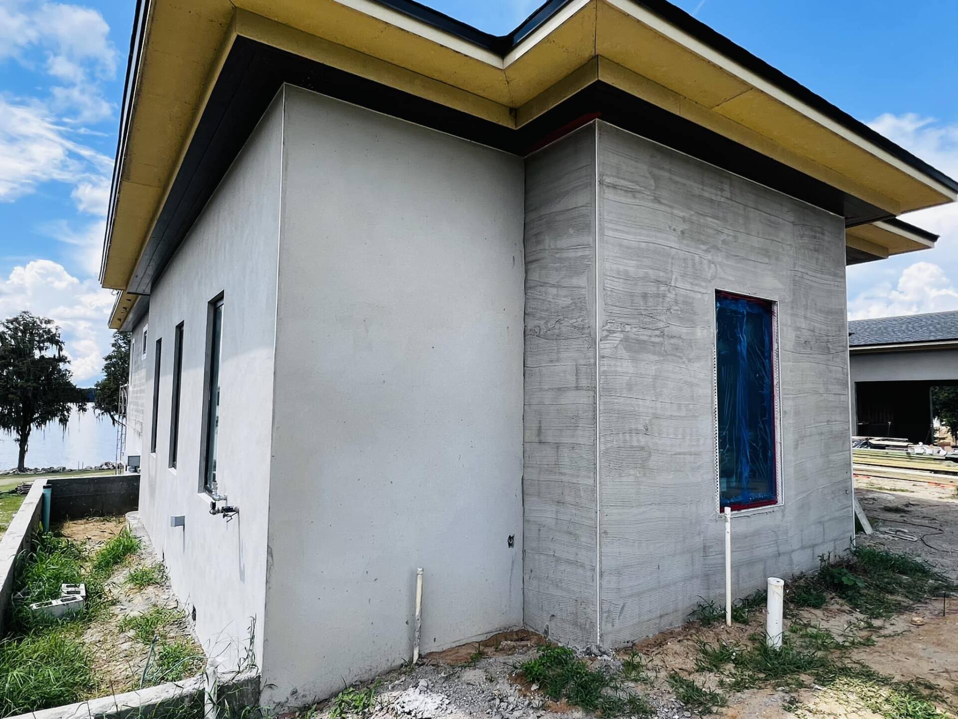 Gray concrete building with dark trim, windows, and a blue door frame under a bright sky.