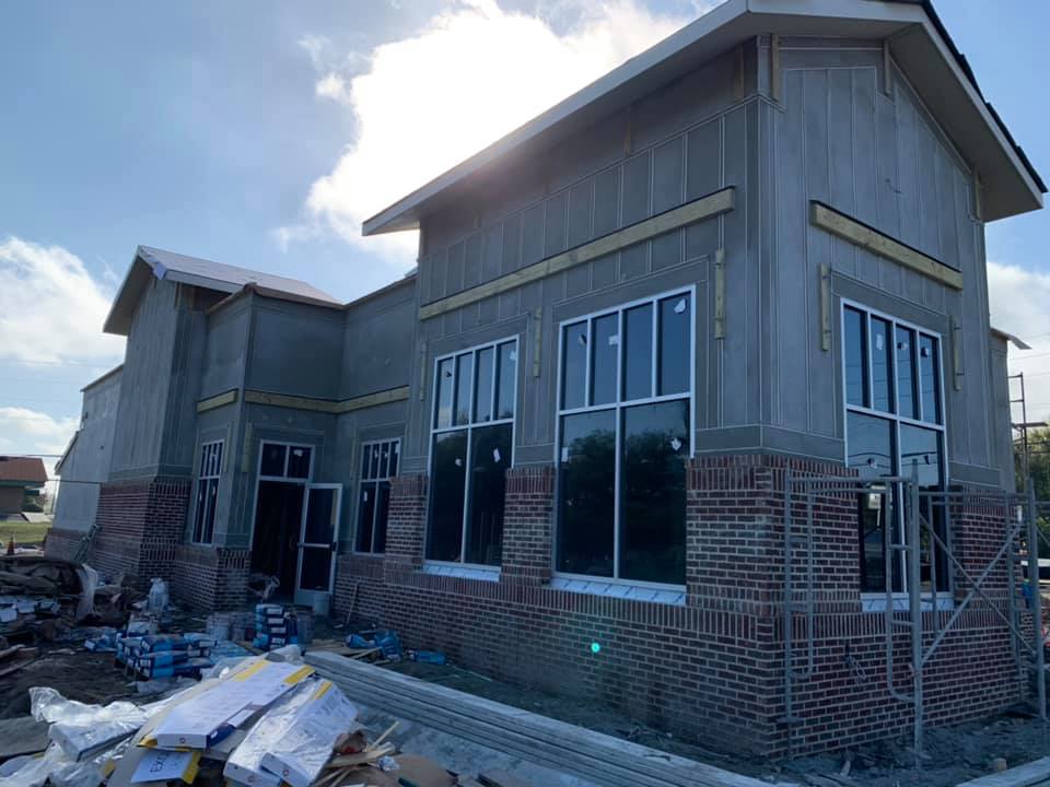 Building under construction with exposed brick, large windows, and unfinished siding.