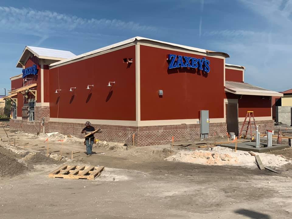 Zaxby's restaurant under construction with red walls, brick base, blue sign, and worker outside.