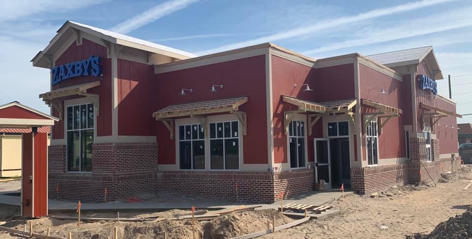 Exterior of a Baker's restaurant under construction; red walls, blue sign, brick accents, dirt, and a clear sky.
