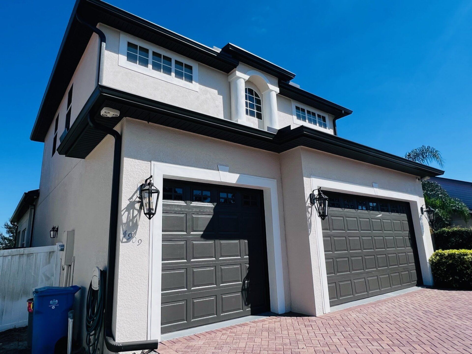 Two-story house with gray garage doors, beige walls, and a blue sky.