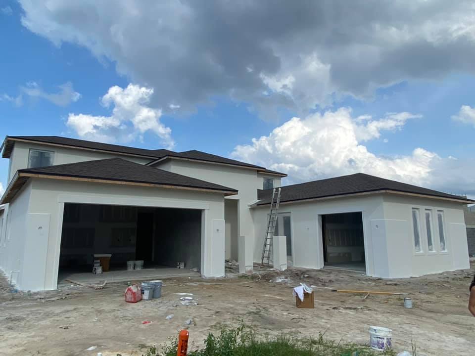 New house under construction, with garages, white exterior, brown roof, blue sky.