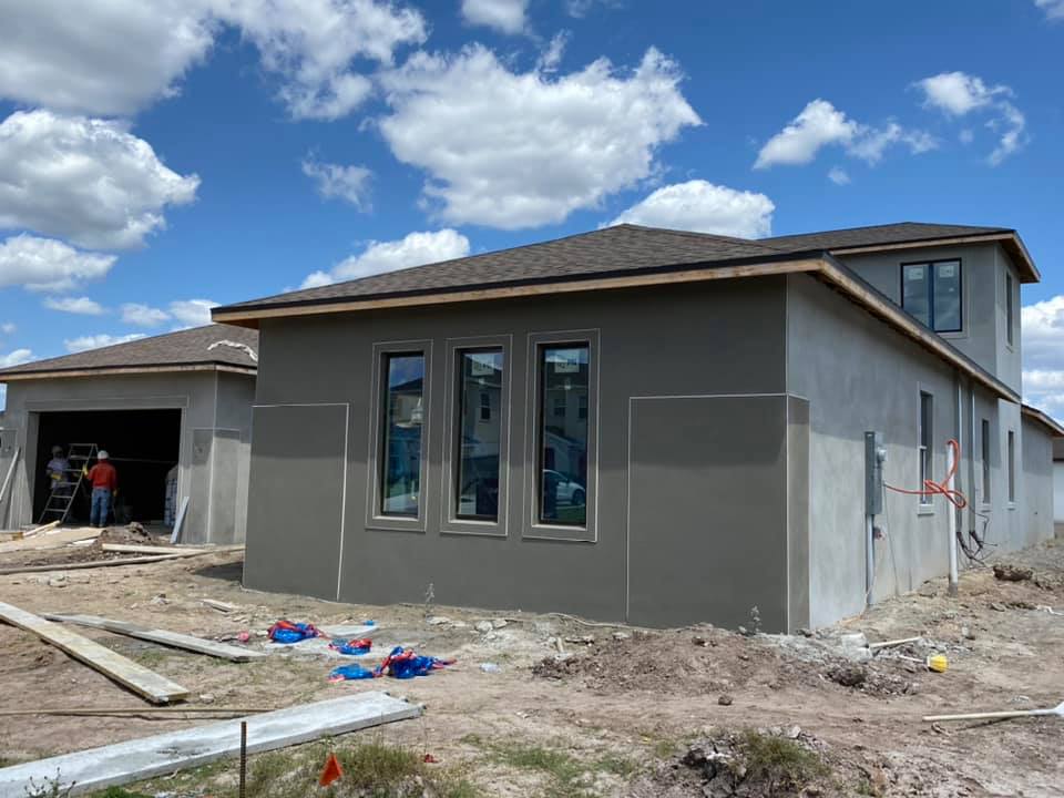 New house under construction, stucco exterior, blue sky, construction workers visible.