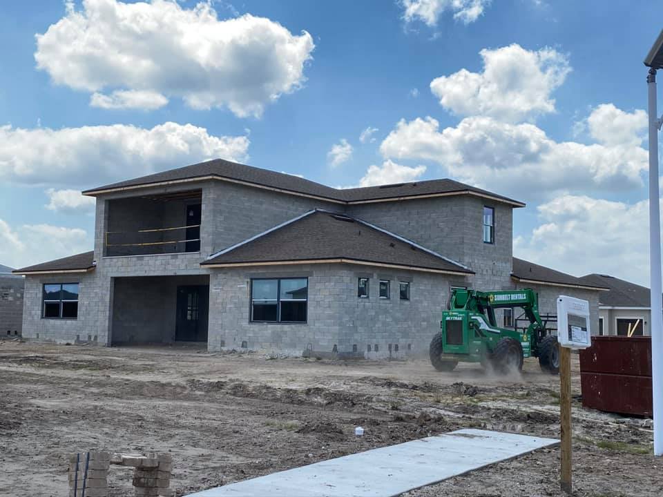 New house under construction; gray brick, brown roof, blue sky, and construction equipment.