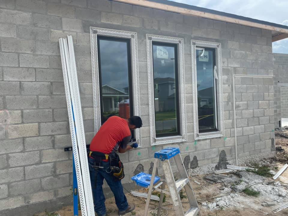 A construction worker installs trim around a window on a cinder block house.