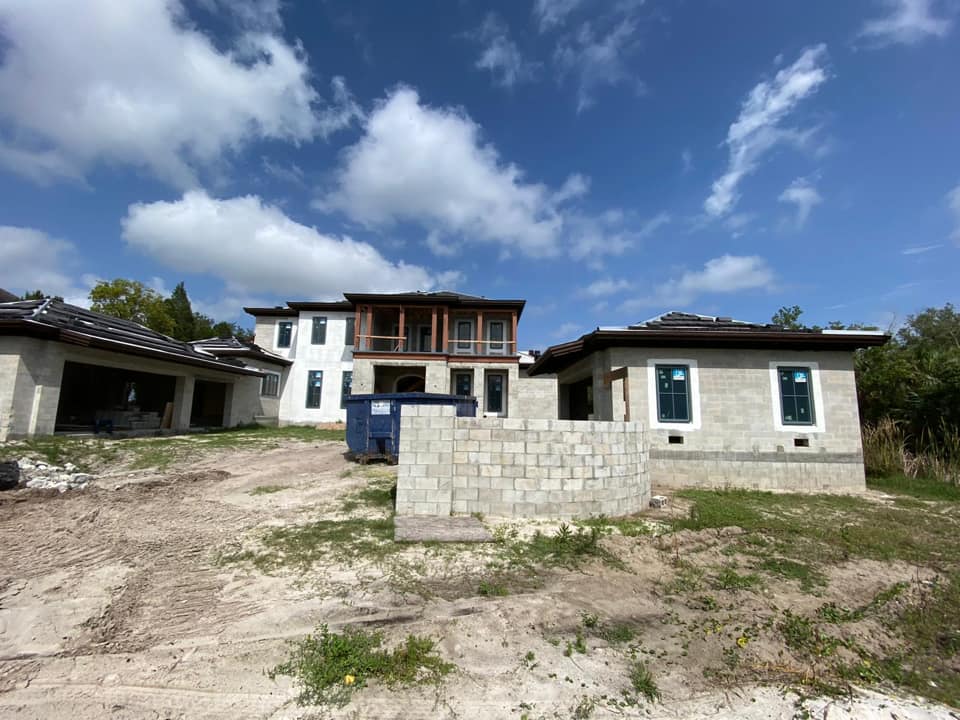 Construction site: multi-story house, stucco walls, concrete block foundation, blue dumpster, blue sky.