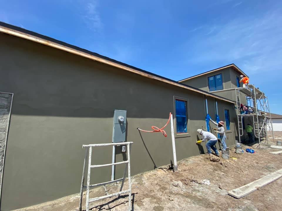 Construction workers applying stucco to a building's exterior under a blue sky.