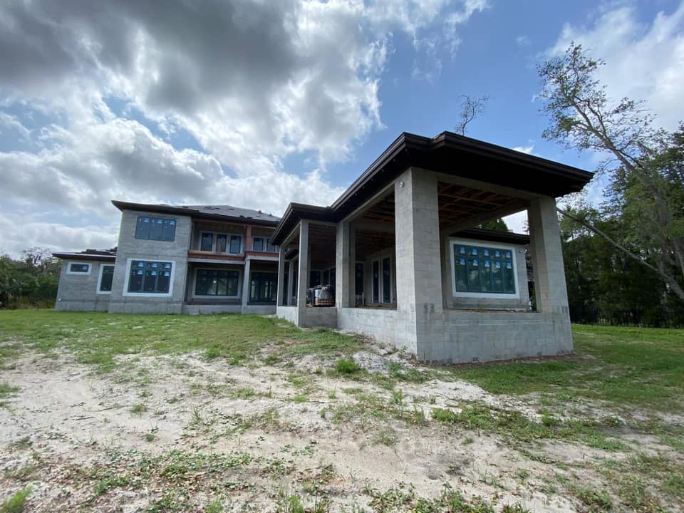 Construction of a large, two-story home with a covered porch, against a cloudy sky.
